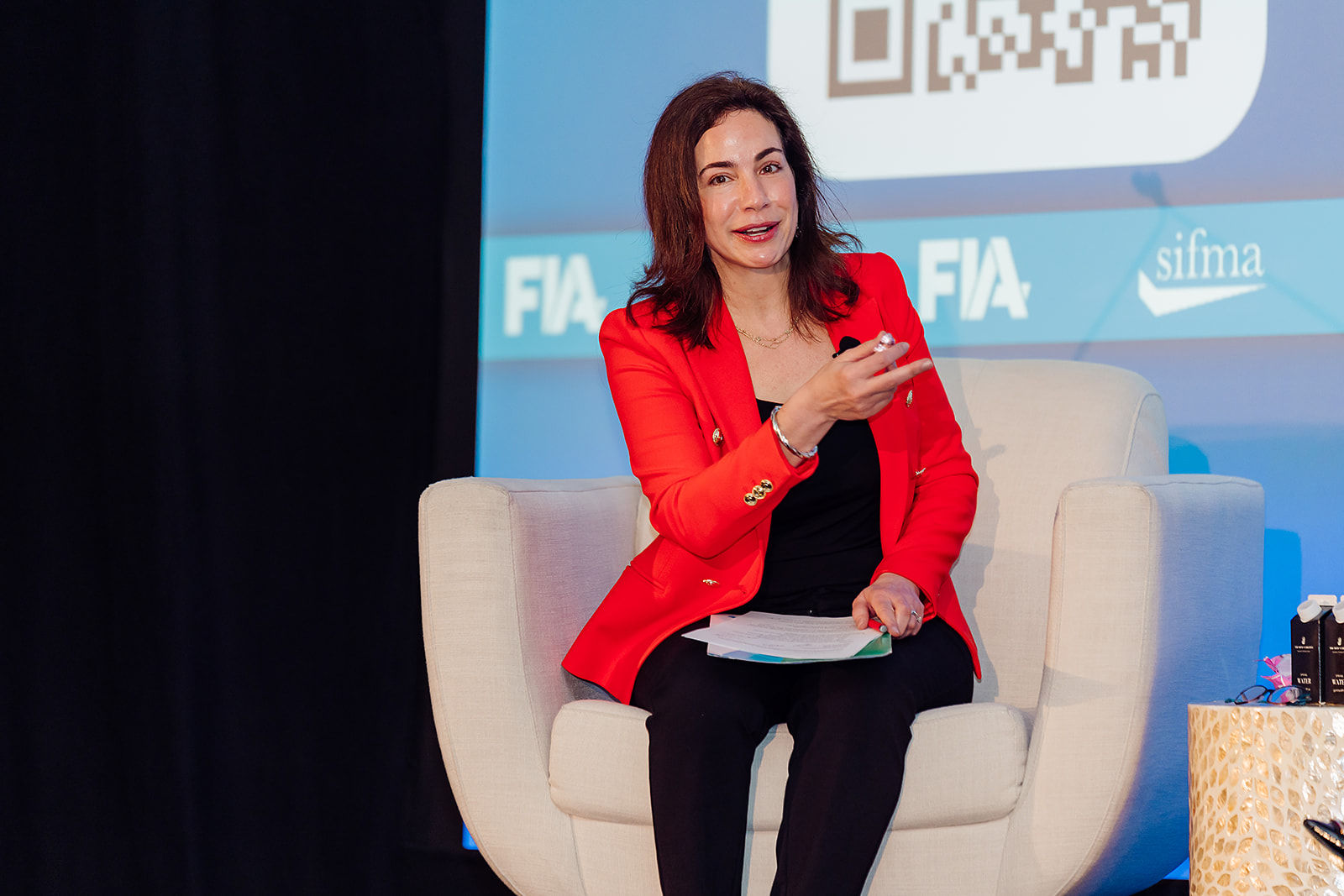 A business leader in a red jacket speaks during an on-stage interview